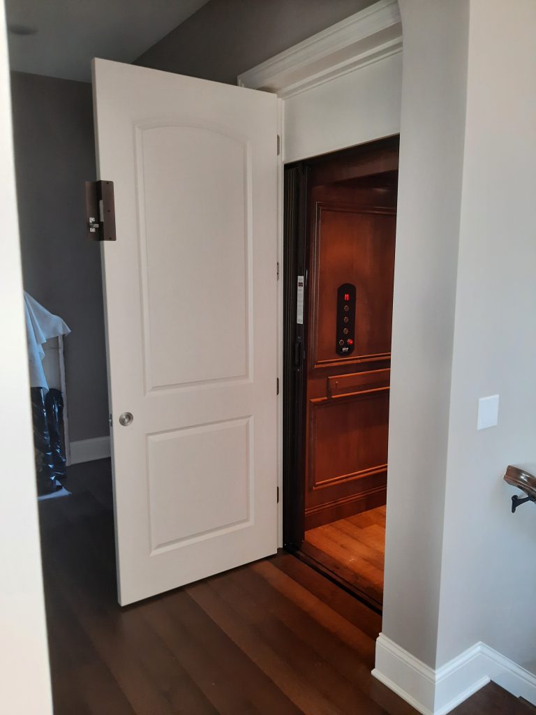 Home Elevator with door open showing interior wood paneling and metal fixtures.